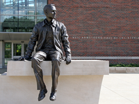 Photo of a statue of Neil Armstrong sitting on a ledge. The words 