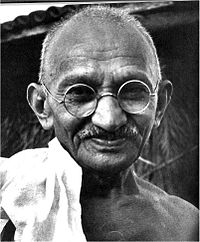 The face of Gandhi in old age—smiling, wearing glasses, and with a white sash over his right shoulder