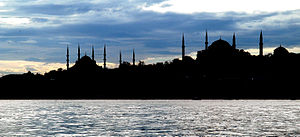 Silhouette of several buildings with domes and spires in front of an open waterway at twilight