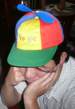 Asian man in his twenties wearing a blue, green, yellow and red propellor hat that says 