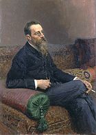 A man with glasses and a long beard sitting on a sofa, smoking