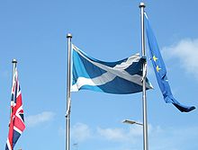 Union Flag, Scottish Flag and European Flag on poles against a blue sky.