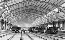 Two trains and two empty rail tracks below an ornate roof which recedes into the distance