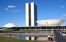  The view shows a 20th century building with two identical towers very close two each other rising from a low building which has a dome at one end, and an inverted dome, like a saucer, at the other.