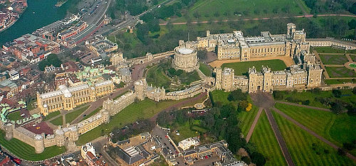 An aerial photograph of a castle, with three walled areas clearly visible, stretching left to right. Straight roads stretch away in the bottom right of the photograph, and a built-up urban area can be seen outside the castle on the left. In the upper right a grey river can just be seen.