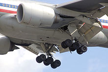 Aircraft belly section. Close view of engines, extended landing gear, and angled control flaps.