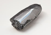 An irregular bar of lustrous silvery metal. One end is rough, as though broken, while the other, cigar-shaped end is relatively smooth.