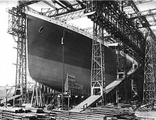 Photograph of a huge gantry with the bow of a large ship that has been painted in dark colours.