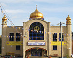 A large symmetrical two-storey building of yellow brick. The centre bay, incorporating the entrance, juts out. It has a large window with a semicircular top on the first floor and above is a golden onion dome on a blue base. At the ends of the frontage are hexagonal pilasters with small octagonal windowed pavilions and onion domes on top. Above the entrance is a white sign saying 