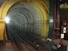 A narrow railway tunnel with a single railway track, lit by a bright white light