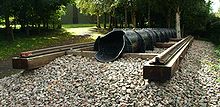 Exterior in woodland. a short section of railway line on wooden sleepers with a cast iron pipe of approximately one foot diameter, running inline with the rails