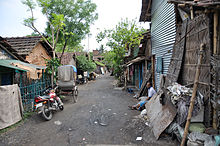 An unpaved road with huts on two sides in a slum area