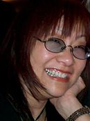 Profile picture of a bespectacled Asian woman in her early fifties. She has long red hair, and shows a toothy smile.
