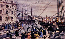 Two ships in a harbor, one in the distance. On board, men stripped to the waist and wearing feathers in their hair are throwing crates overboard. A large crowd, mostly men, is standing on the dock, waving hats and cheering. A few people wave their hats from windows in a nearby building.