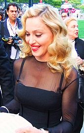 A blond woman in a black dress, smiling and looking down.