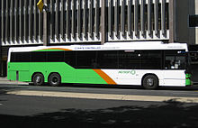 Luz verde, naranja y blanco bus parar en frente del edificio de varios pisos.