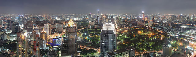 Fotografía panorámica nocturna que muestra un paisaje urbano expansivo con varios rascacielos en el primer plano, un parque en el centro, y un gran grupo de edificios en todo el parque