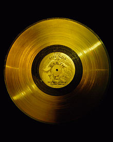 Disco circular plano de oro, con un marcador central, un agujero, y una banda ancha de líneas muy pequeños, como una versión de oro de un viejo disco analógico
