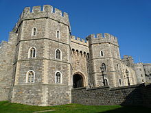 A photograph of a stone gatehouse, with angular octagonal towers and windows picked out in white stone. The weather is good, with the sky behind the gatehouse a bright blue.