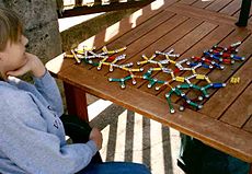 Niño sentado frente a 3/4 de distancia de la cámara, mirando un modelo de bola y el palo de una estructura molecular. El modelo está hecho de los imanes de colores y bolas de acero.