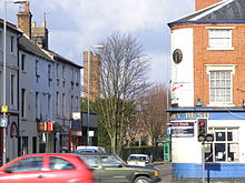 La esquina de una calle con un pub llamado The Ivy Bush en el lado derecho. En el fondo de dos torres de ladrillo de altura se pueden ver más a la izquierda.