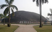 Una gran colina detrás de dos palmeras y un bulevar, gente caminando son alrededor de una quinta altura de la colina