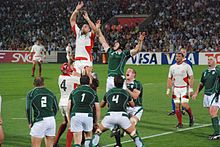 Dos filas de los jugadores rivales, verdes a primer plano, blanco detrás, cada ayuda un jugador que salta de su equipo por levantándolo hacia una pelota-foto colgantes.