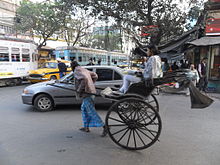 Una intersección congestionada mostrando diferentes vehículos como un rickshaw tirado a mano, taxis, tranvías y coches