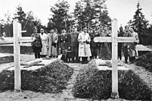 17 hombres, la mayoría en uniforme militar, de pie en un cementerio, ver dos tumbas.