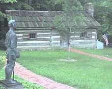 Una cabaña de madera con una estatua y un árbol frente