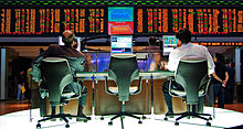 Dos hombres se sientan en monitores de ordenador con la información financiera