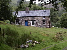 Una fotografía de color de una casa de piedra en una colina