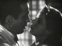 Blanco y negro película de captura de pantalla de un hombre y una mujer como se ve desde los hombros hacia arriba. Los dos están cerca uno del otro como si fuera a besar.