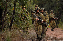 Un grupo de soldados australianos con fusiles en movimiento a lo largo de un camino en una zona boscosa