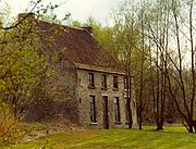 foto de una casa de ladrillo de dos pisos de la izquierda parcialmente oscurecida por los árboles con un jardín delantero y con una hilera de árboles a la derecha