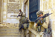 photographie de trois Marines entrer dans un palais en pierre partiellement détruit avec une peinture murale de l'écriture arabe