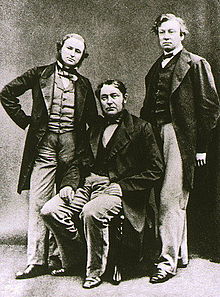 Trois hommes d'âge moyen, avec l'une au milieu assis. Tous portent des vestes longues, et l'homme court sur la gauche a une barbe.