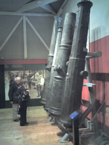 Une vue de quatre très gros canons se penchant vers la paroi intérieure d'un bâtiment avec un plafond haut