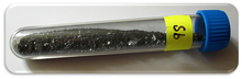 Un flacon transparent contenant de petits morceaux d'un peu noir lustré solide, marqué