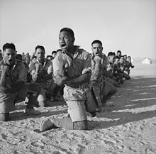 Une escouade d'hommes à genoux dans le sable du désert tout en effectuant une danse de guerre