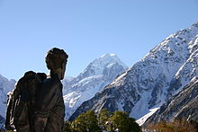 Dark statue with backpack facing a snow capped mountain