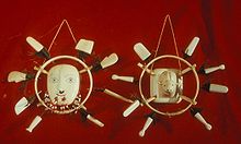 Photo de deux masques: Dans le centre est l'image d'un visage, entouré par un anneau, à son tour entouré de huit pièces rectangulaires blanches.