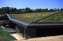 Un bâtiment bas a un toit entièrement recouvert avec de la terre et de l'herbe. Il semble être construit sur une colline