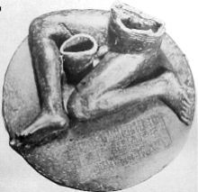 Photographie en noir et blanc d'une statue constitué d'un inscrit, Guéridon rond au sommet de laquelle se trouve une, nue, figure masculine assise dont seulement les jambes et le bas du torse sont préservés