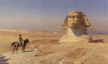 Personne sur un cheval regarde vers une statue géante d'une tête dans le désert, avec un ciel bleu