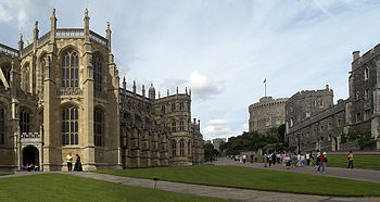 Une photographie d'une grande chapelle gothique sur la gauche, avec des fenêtres grand et mince. Sur la droite est une ligne de bâtiments en pierre, pointant vers une tour circulaire au milieu de l'image. Au centre se trouvent deux chemins entourés par de l'herbe, avec un certain nombre de gens se promener.