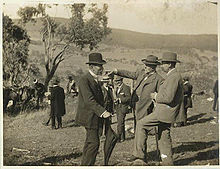 Trois hommes d'âge moyen avec des barbes courtes en costumes et chapeaux formels permanents dans le domaine vallonné ouverte avec un seul arbre à proximité