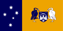 Left third: White stars of the Southern Cross on blue field.  Right two-thirds; black and white swans holding a blue shield with a white castle above a white flower and below a sword and scepter arranged in an