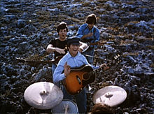 Les Beatles jouant de la musique dans un champ. Au premier plan, les tambours sont joués par Starr (seul le haut de sa tête est visible). Au-delà de lui, les trois autres se tiennent dans une colonne avec leurs guitares. À l'arrière, Harrison, tête en bas, touche une corde sensible. À l'avant, Lennon sourit et donne un petit signe vers la caméra, tenant son choix. Entre eux, McCartney est en plaisantant sur le point de se étouffer Lennon.