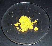 Certains poudre jaune canari se trouve, la plupart en morceaux, sur un verre de montre de laboratoire.